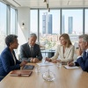 A group of four professionals engaged in a discussion around a conference table with a city skyline visible through large windows.
