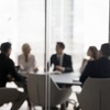 Blurred image of a group of professionals in a meeting around a table in a modern office.