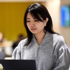 A woman works intently on a laptop in a busy office environment.