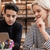 Two young people are collaborating on a laptop in a cozy study environment.