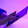 A person using a laptop in a room illuminated by purple light.