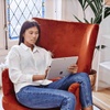 A woman sits on a red chair using a tablet in a stylishly decorated room.