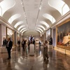 A spacious art gallery featuring large paintings and visitors exploring the exhibits.