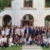 A large group of students posing for a photo with a few adults in front of a building with a classic facade and green lawn.