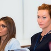 Two women attentively participating in a seminar, one with auburn hair and the other wearing glasses.