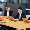 Four business professionals working and discussing around a table in a modern office setting.