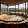 A modern round conference room with a large wooden table and panoramic views of nature.