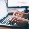 Person typing on a laptop with another monitor in the background.