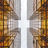 Looking upward between two symmetrical skyscrapers with a clear sky above and reflections on the glass facade.