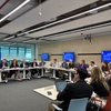 A conference room filled with professionals discussing various topics around a large table.