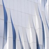 The image features a modern architectural facade with flowing, wave-like patterns in shades of white and blue.