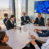 A group of students engaged in a discussion with a professor in a modern classroom setting with a city view.