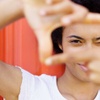 A young person with an afro smiling and making a frame with their hands in front of a red background.