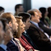 A group of people sitting in a row at a conference, focused attentively forward.