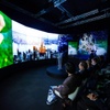 People sitting in a dark room watching a panoramic display showing vibrant images of nature and cities.