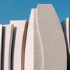 A modern architectural structure with abstract, wave-like surfaces against a blue sky.