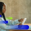 A woman is using a tablet at a desk with a cup next to her.