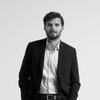 A black and white photo of a young man in a suit standing with his hands in his pockets.