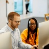 A man and a woman working together on computers in a modern office setting.