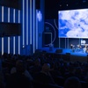 An auditorium filled with an audience watching a presentation on a large screen.