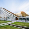 Modern architectural building featuring an angular design and a predominantly white facade, surrounded by a green lawn and a pedestrian walkway.