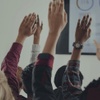 A group of people raising their hands in a classroom setting during a presentation.