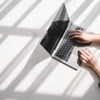 A person typing on a laptop with sunlight casting shadows onto the surface.