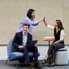 Three colleagues are engaging in a positive interaction in a modern office setting.
