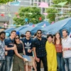 A diverse group of people smiling at an outdoor event with tents and hanging flags.