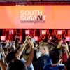 A vibrant crowd holding smartphones at a large event with a prominent stage display.