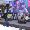 A panel discussion taking place with several speakers sitting on stage and flags in the background.
