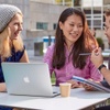 Three IE students speaking outside sitting on a table with a computer