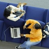 Two people sitting on a blue sofa, one working on a laptop and the other using a smartphone.