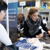 Two women are engaging at a professional event, discussing ideas while examining a laptop.