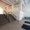 A modern interior space featuring a staircase with grey steps, white walls, and exposed red ceiling pipes.