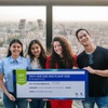 A group of four young adults celebrating their first place win at a tech bootcamp event in a cityscape setting.