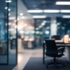 A dimly lit office space with a blurred perspective, featuring an empty chair and illuminated workstations in the background.