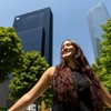 A young woman is smiling joyfully in front of tall buildings on a sunny day.