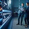 Two colleagues are discussing data on a digital display in a modern office environment.