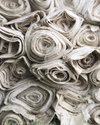 The image shows a stack of rolled fabric in neutral tones.