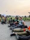 A group of people wearing green vests sit on the ground in a training or outdoor setting.