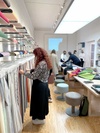 A woman browsing through fabric swatches in a modern textile store with other customers and staff in the background.