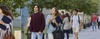 A group of young adults walking on a college campus, some engaged in conversation and others looking ahead.