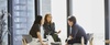 Three colleagues are engaged in a conversation in a bright, modern office space.