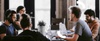 A group of people working together in a modern office environment with laptops and headphones.