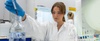 A woman in a laboratory is carefully adding a liquid from a pipette into a container.