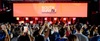 A vibrant crowd holding smartphones at a large event with a prominent stage display.