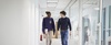 Two young people are walking together in a modern hallway.