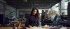 A woman working attentively at a drafting table in an industrial workspace filled with various design materials.