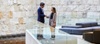 A man and a woman are shaking hands in a modern office lobby with stone walls and contemporary furniture.